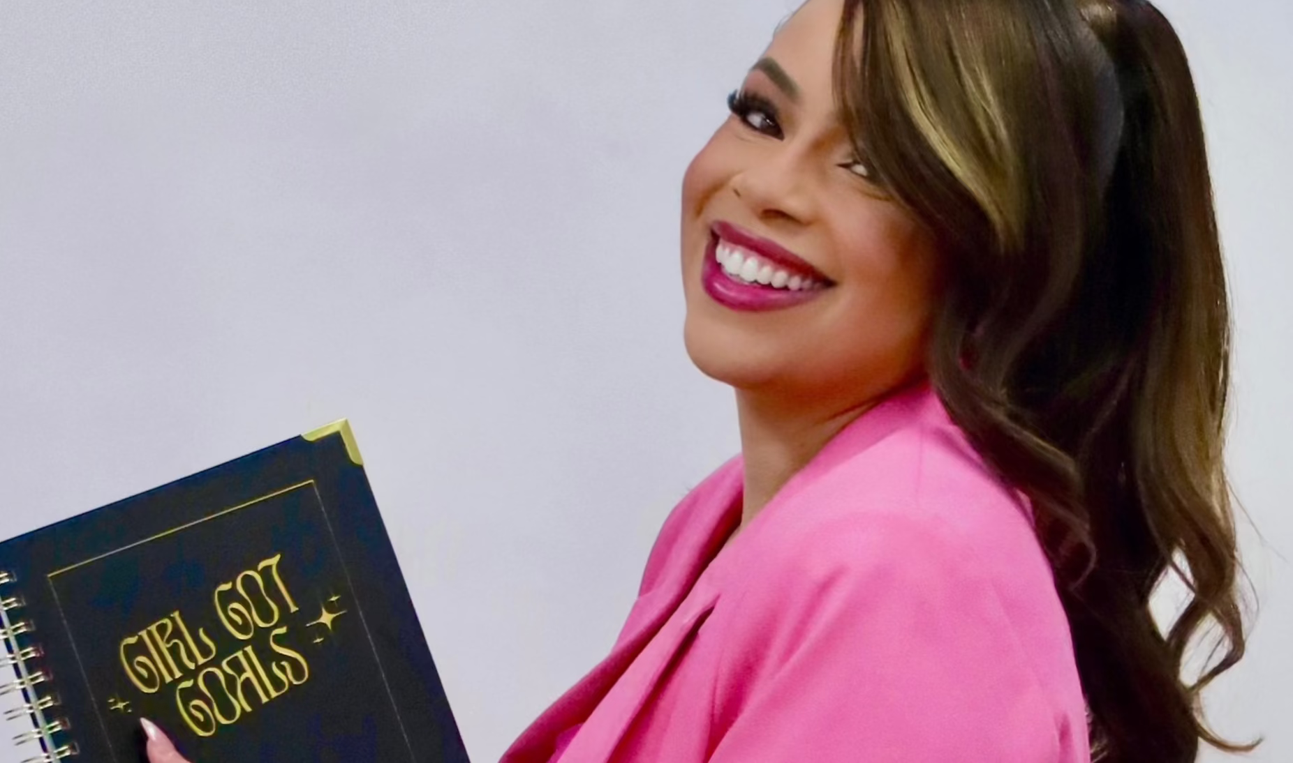 Woman in a pink blazer holding a black book on a white background