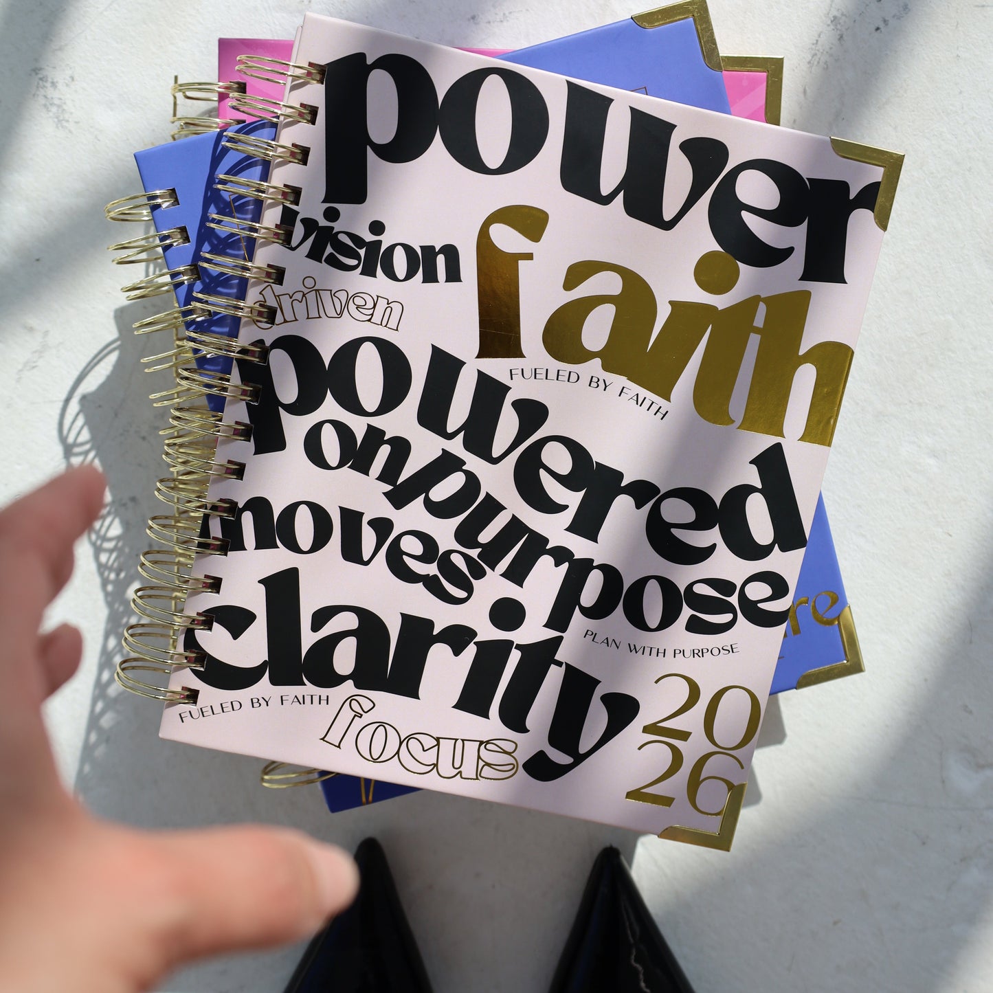 Stack of motivational books on a textured surface with a hand pointing to one of them.