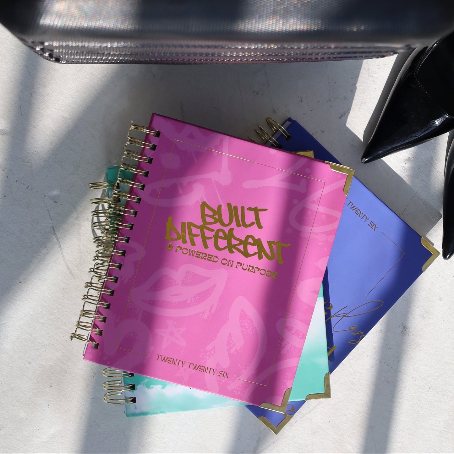 Black handbag, black high-heeled shoes, and colorful notebooks on a white surface.